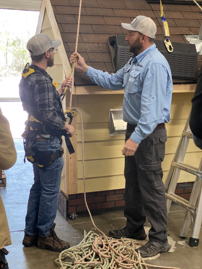 Two men are holding onto a rope affixed to the roof of a scale building.